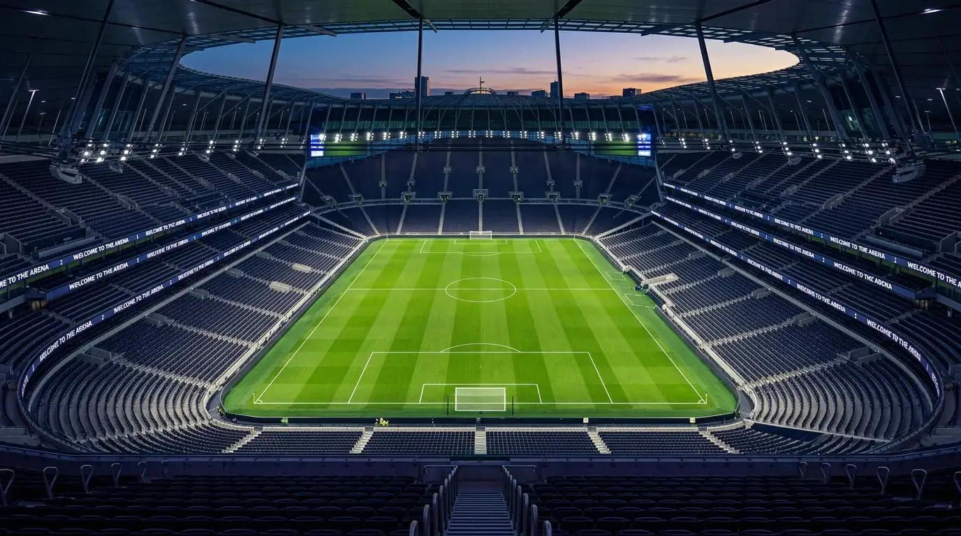 Empty Premier League stadium at dusk with deserted stands and lit pitch view from a high gantry